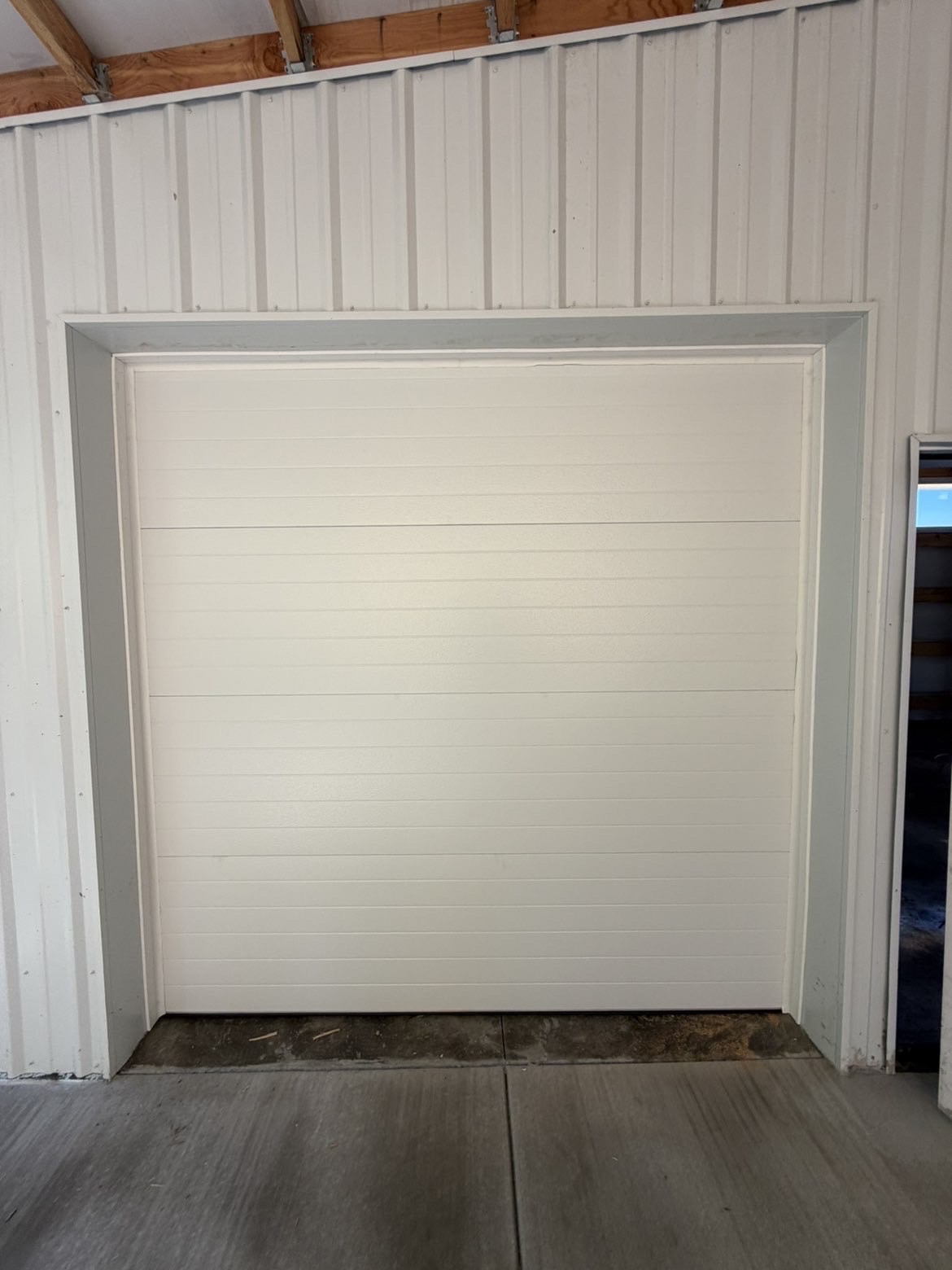 Flush white sectional garage door in a white steel building