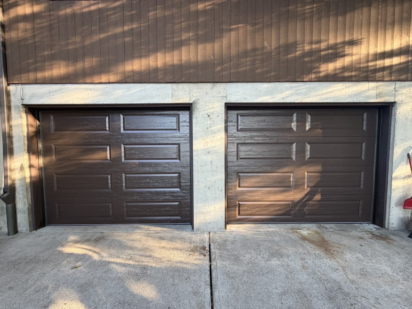 Two brown woodgrain garage doors on a concrete and wood home