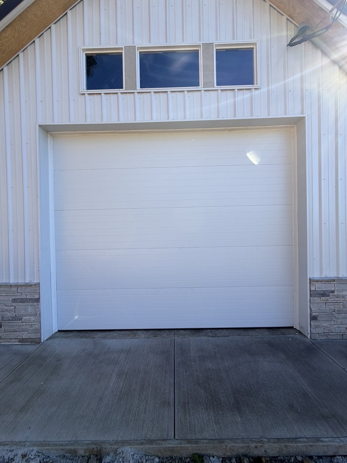White sectional garage door with window row on a white metal shop building