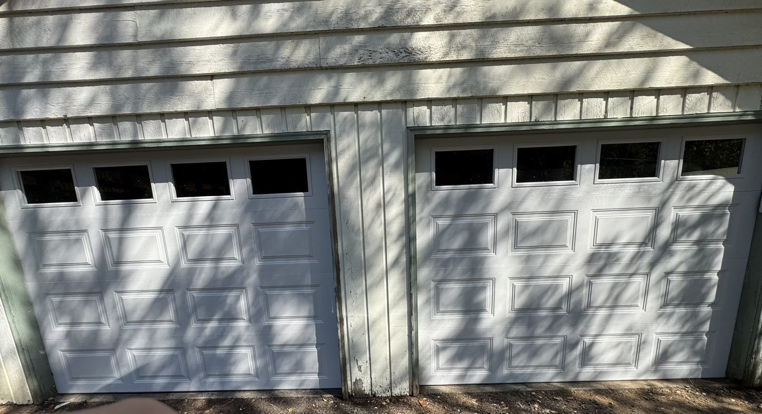 Two white short-panel garage doors with window rows on a home